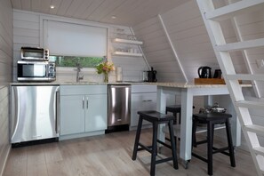 A modern kitchen with stainless steel appliances, a wooden floor, and a white interior.