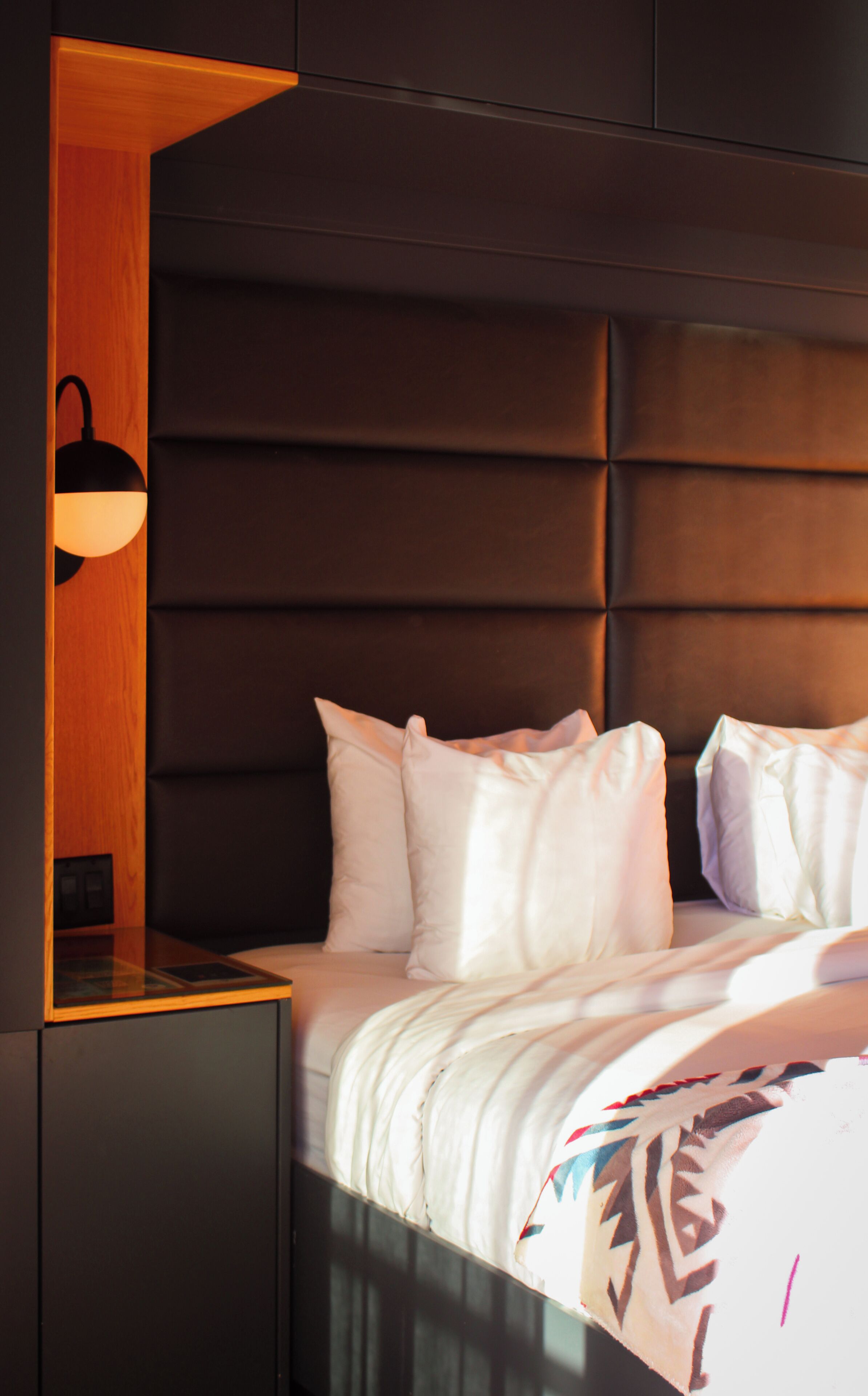 A neatly made bed with white linens, a dark headboard, and a bedside table with a lamp.