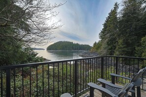 A deck with chairs overlooking a lake, surrounded by trees. - Duffin Cove Oceanfront Lodging (Tofino)