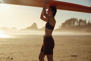A person holding a surfboard on a beach with trees in the background.
