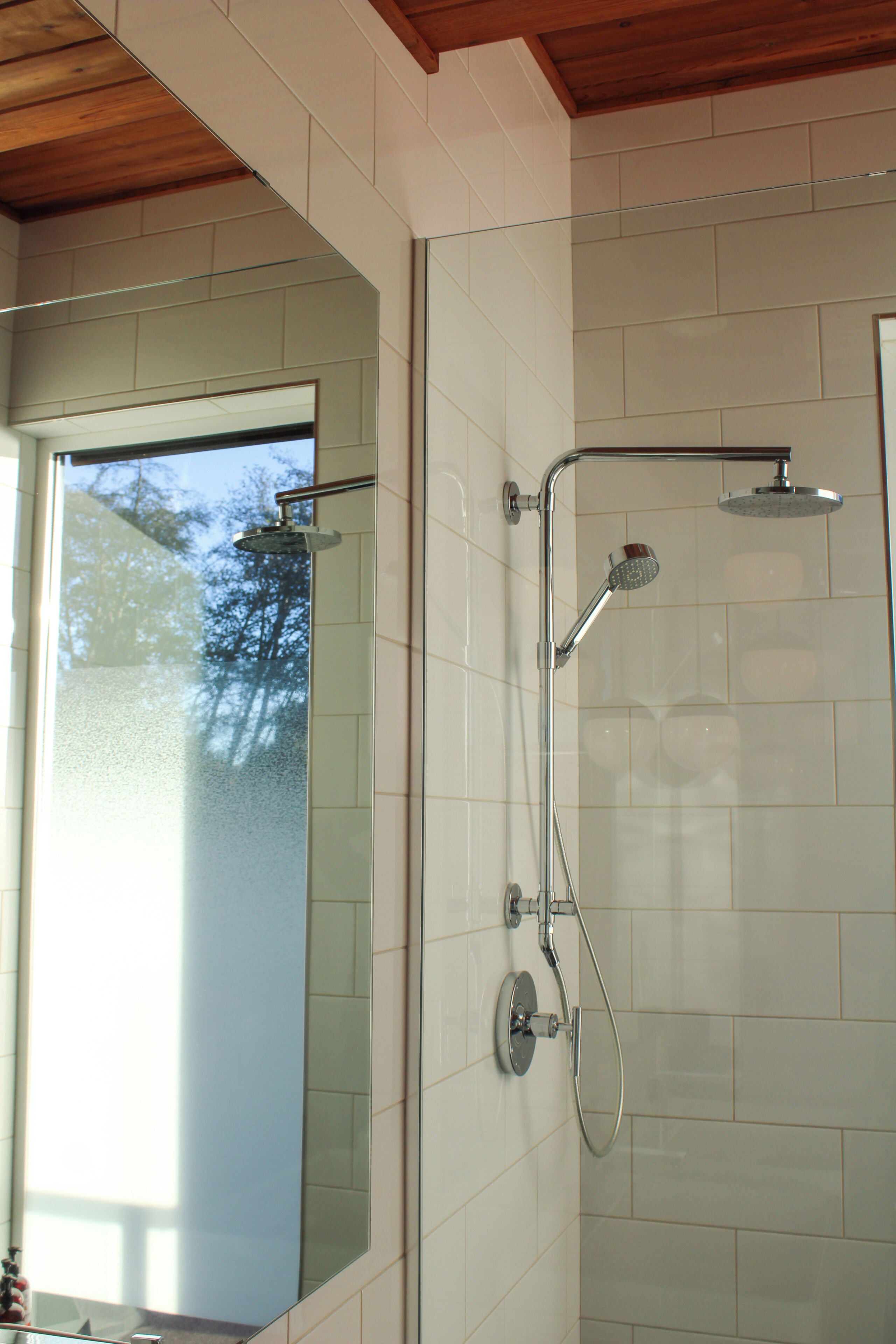 A shower with a glass door, a handheld showerhead, and a wall-mounted showerhead.