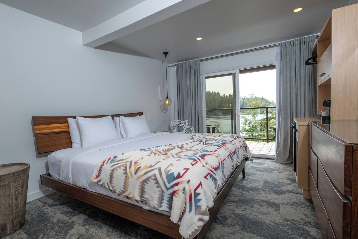 A modern hotel room with a large bed, a balcony with a view, and a wooden dresser.