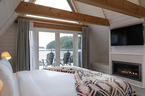 Une chambre à coucher avec un lit, une cheminée, une télévision et un balcon équipé de chaises.