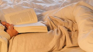 Una persona leyendo un libro en una cama con vistas al verdor exterior.
