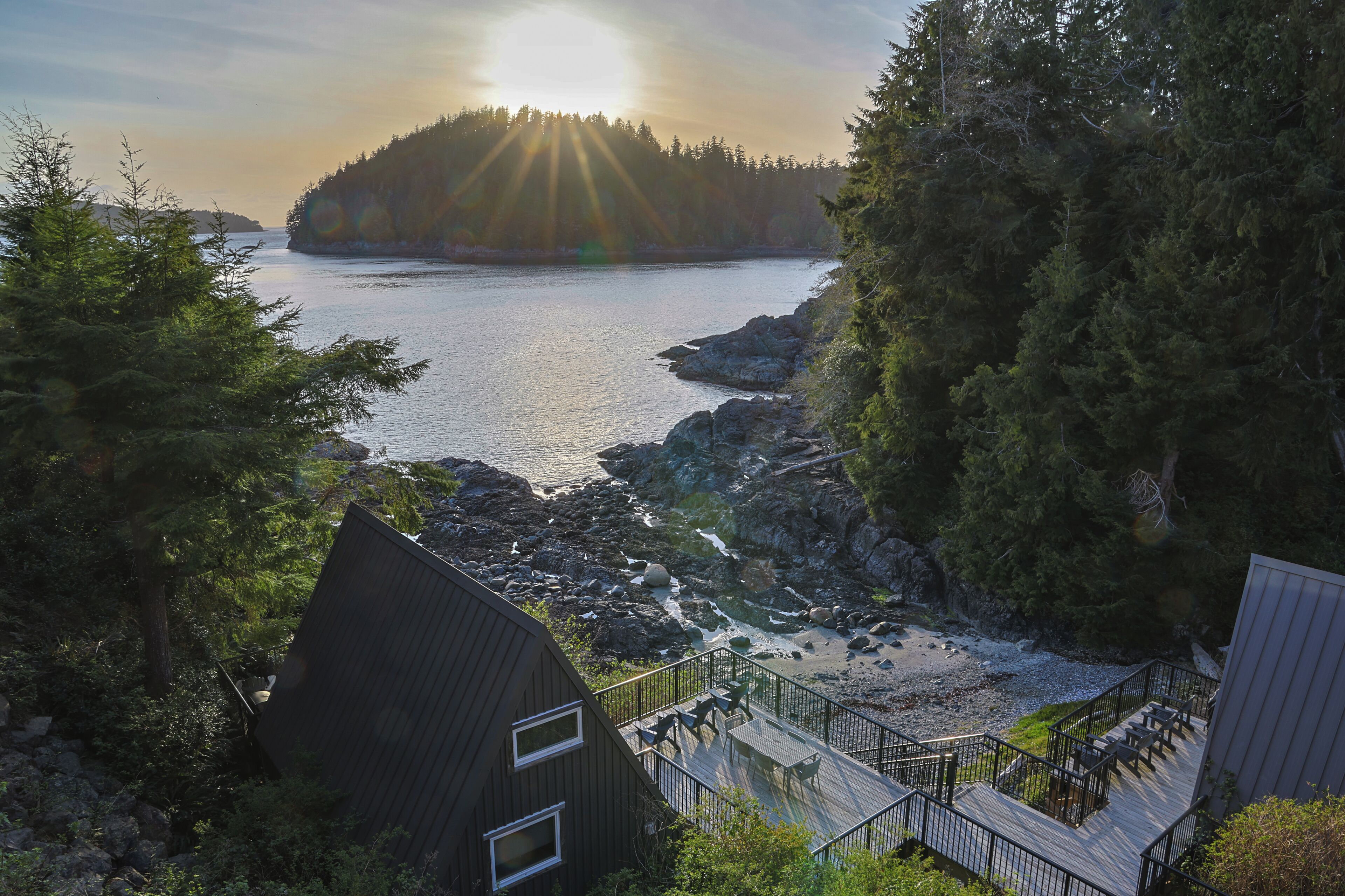 A coastal property with a deck, a view of the sea, and a forested area.