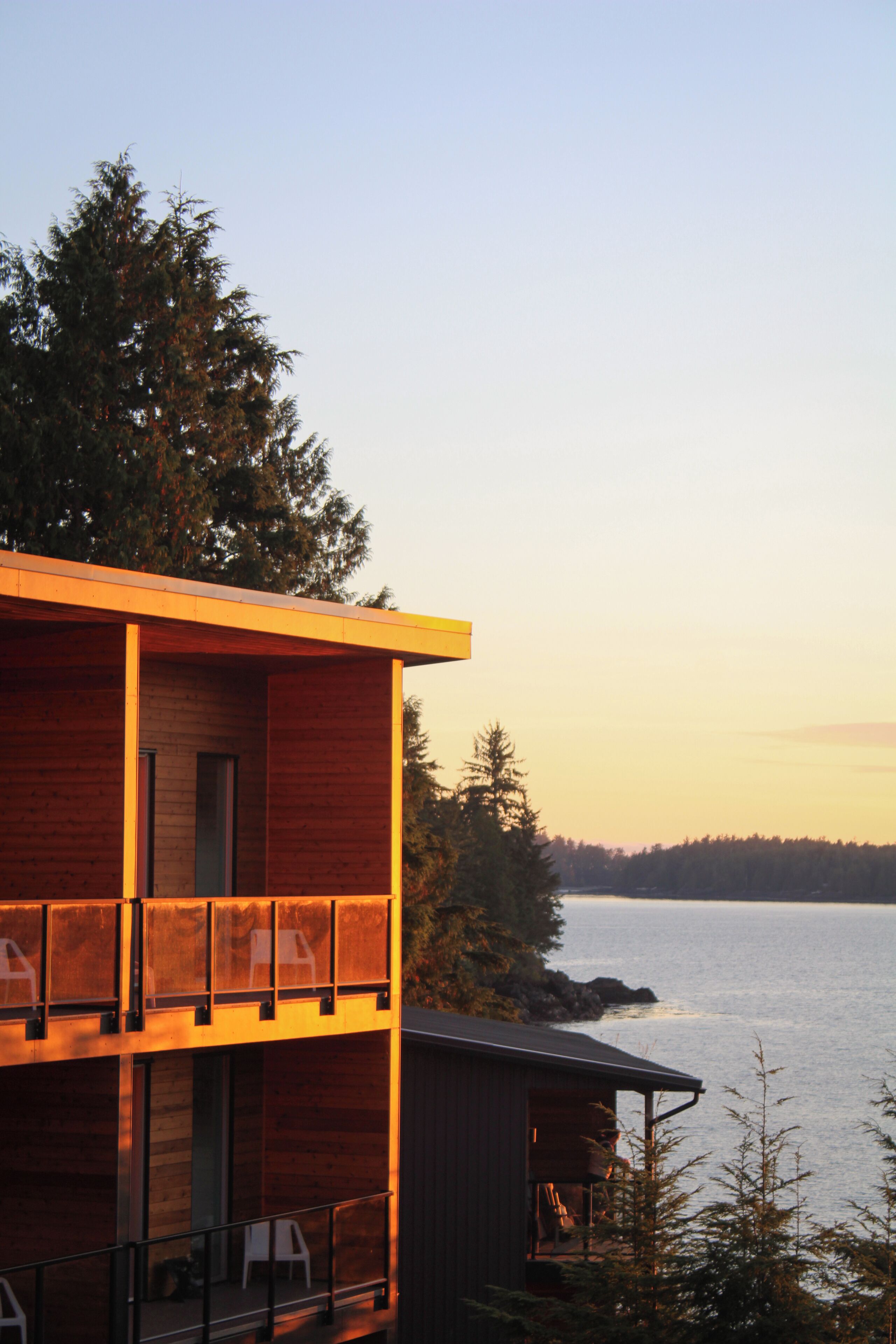 A modern wooden cabin with a balcony overlooking a body of water.