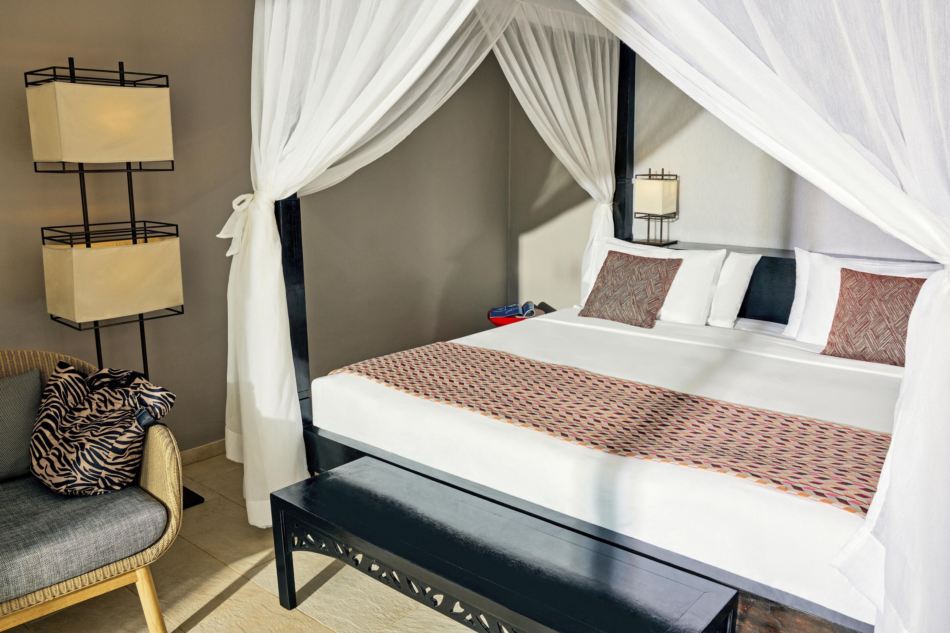 A bed with a canopy, a bedside table, a chair, and a floor lamp.