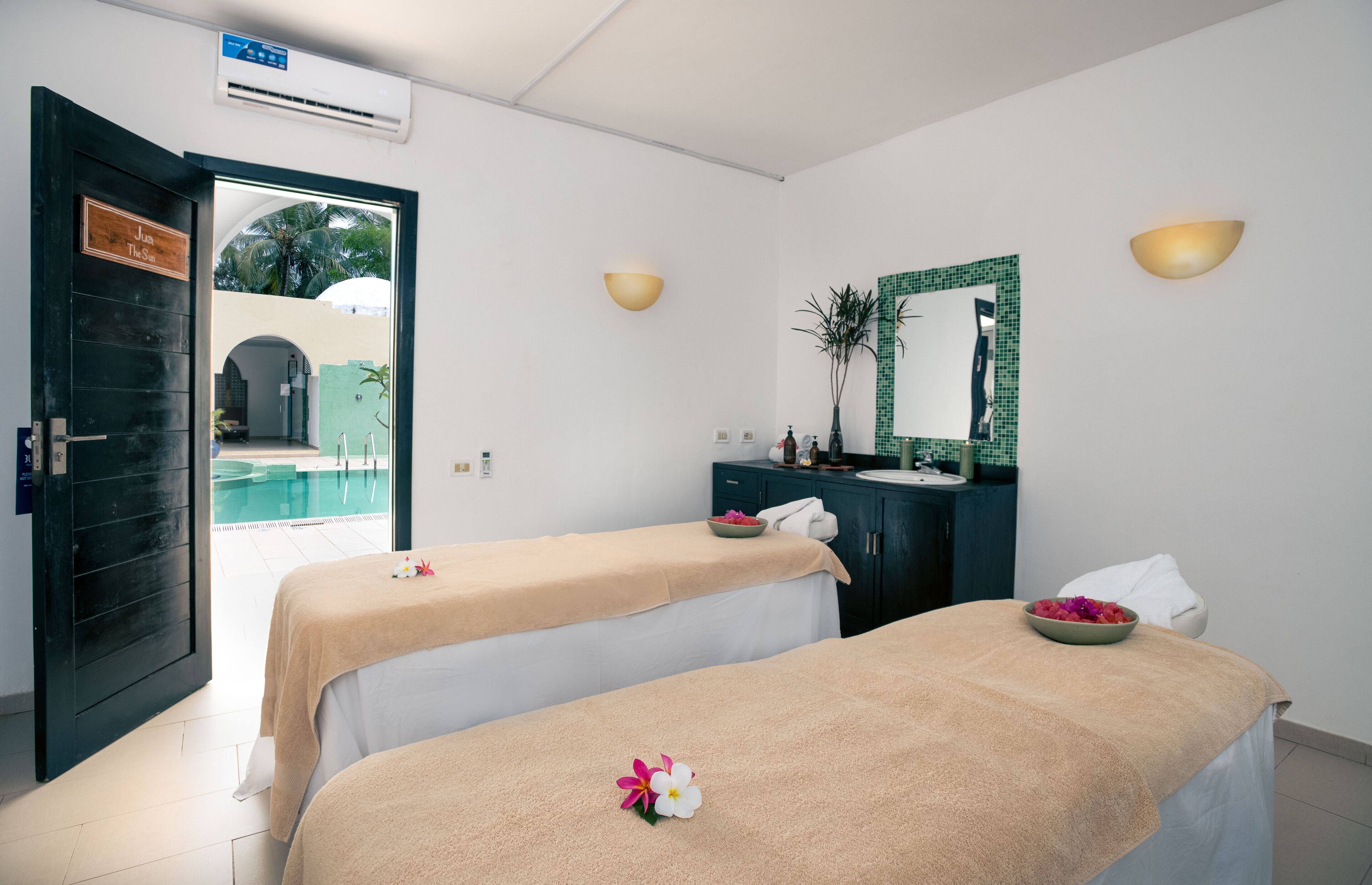Ein Spa-Raum mit zwei Massagetischen, einem Spiegel und Blick auf ein Außenbecken.