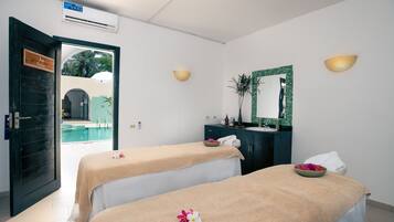 A spa room with two massage tables, a mirror, and a view of an outdoor pool.