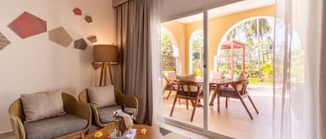 A room with a sofa, a coffee table, and a view of an outdoor patio with chairs and a table.