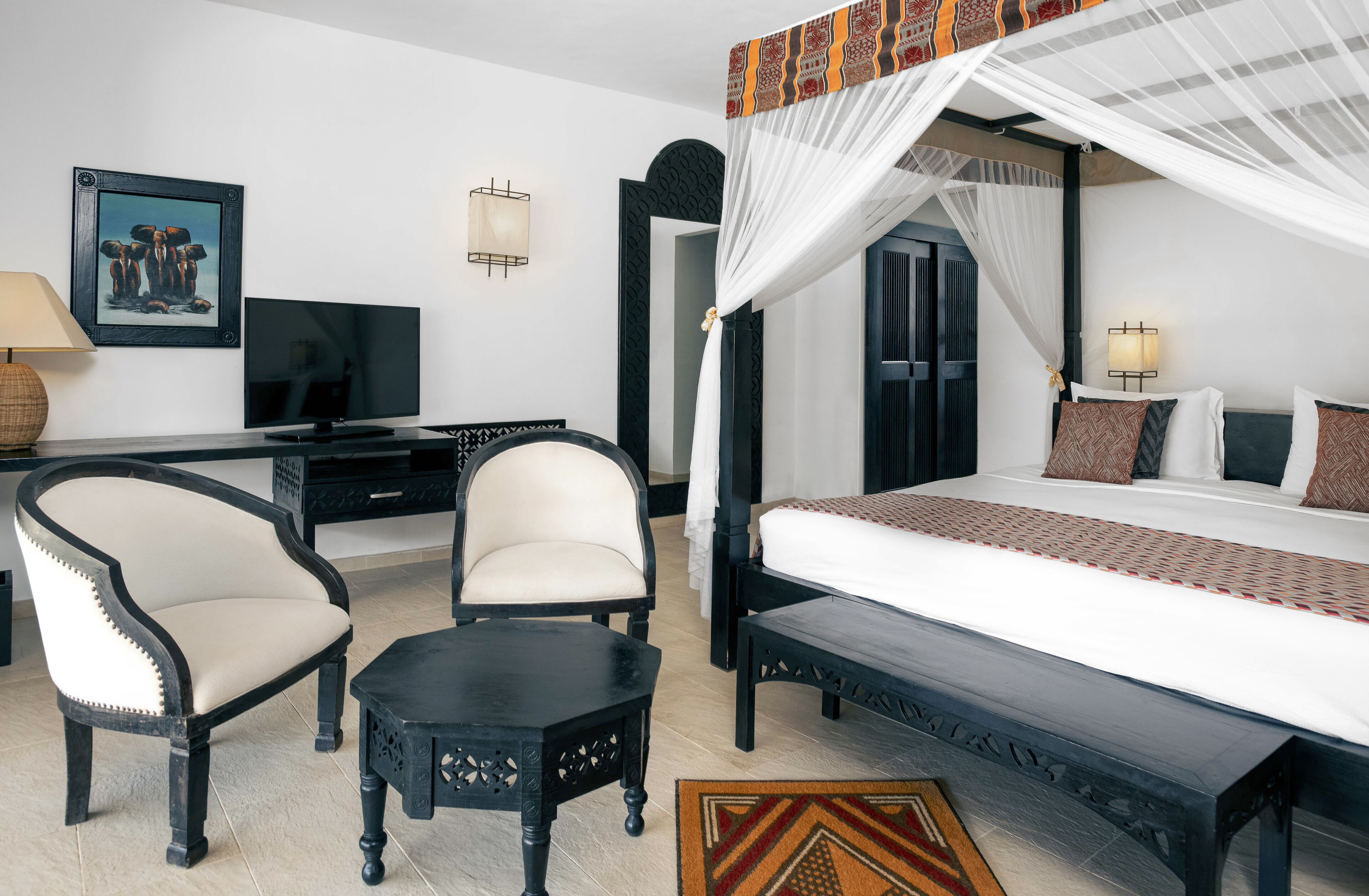 Una habitación de hotel con cama, dos sillas, escritorio con televisor y un ventanal grande.