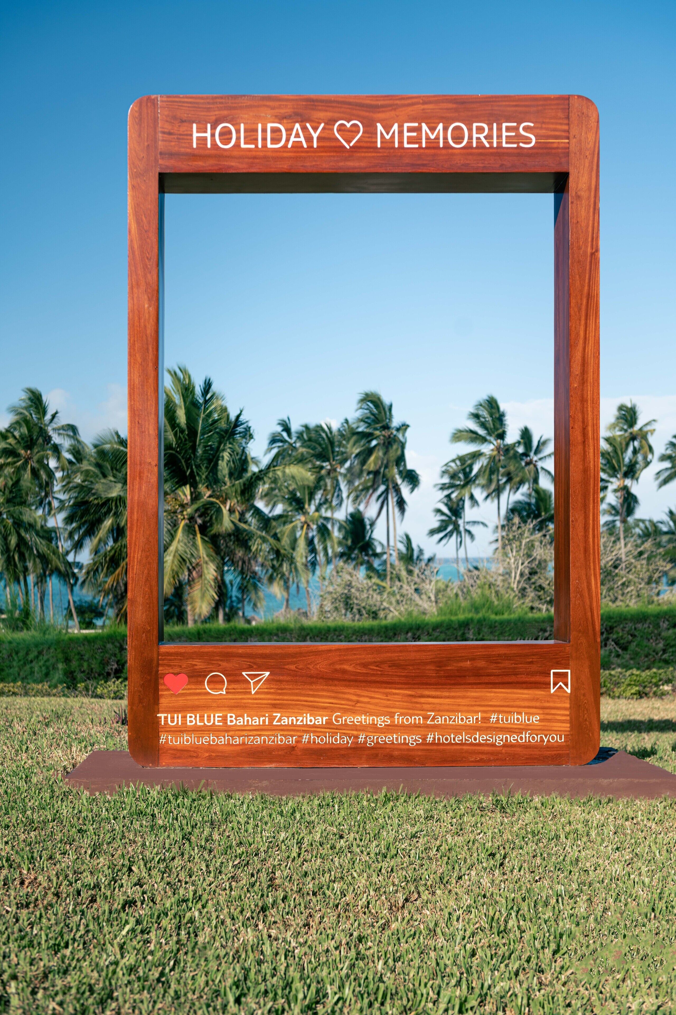 A wooden frame with the text "HOLIDAY MEMORIES" and "TUI BLUE Bahari Zanzibar Greetings from Zanzibar!" on a grassy area with palm trees in the background.