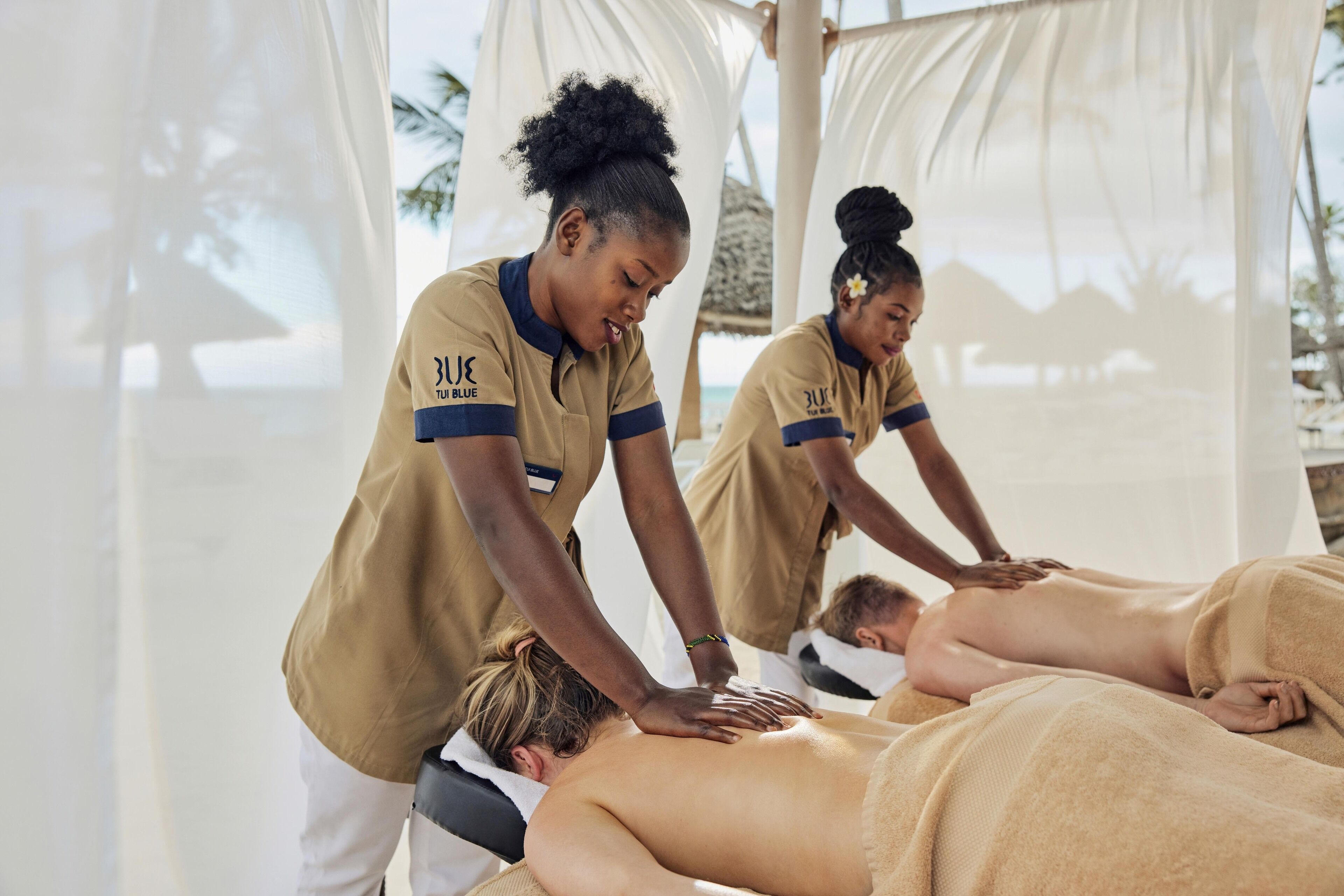 A massage therapy session in a beachside setting with a thatched roof and white drapes.