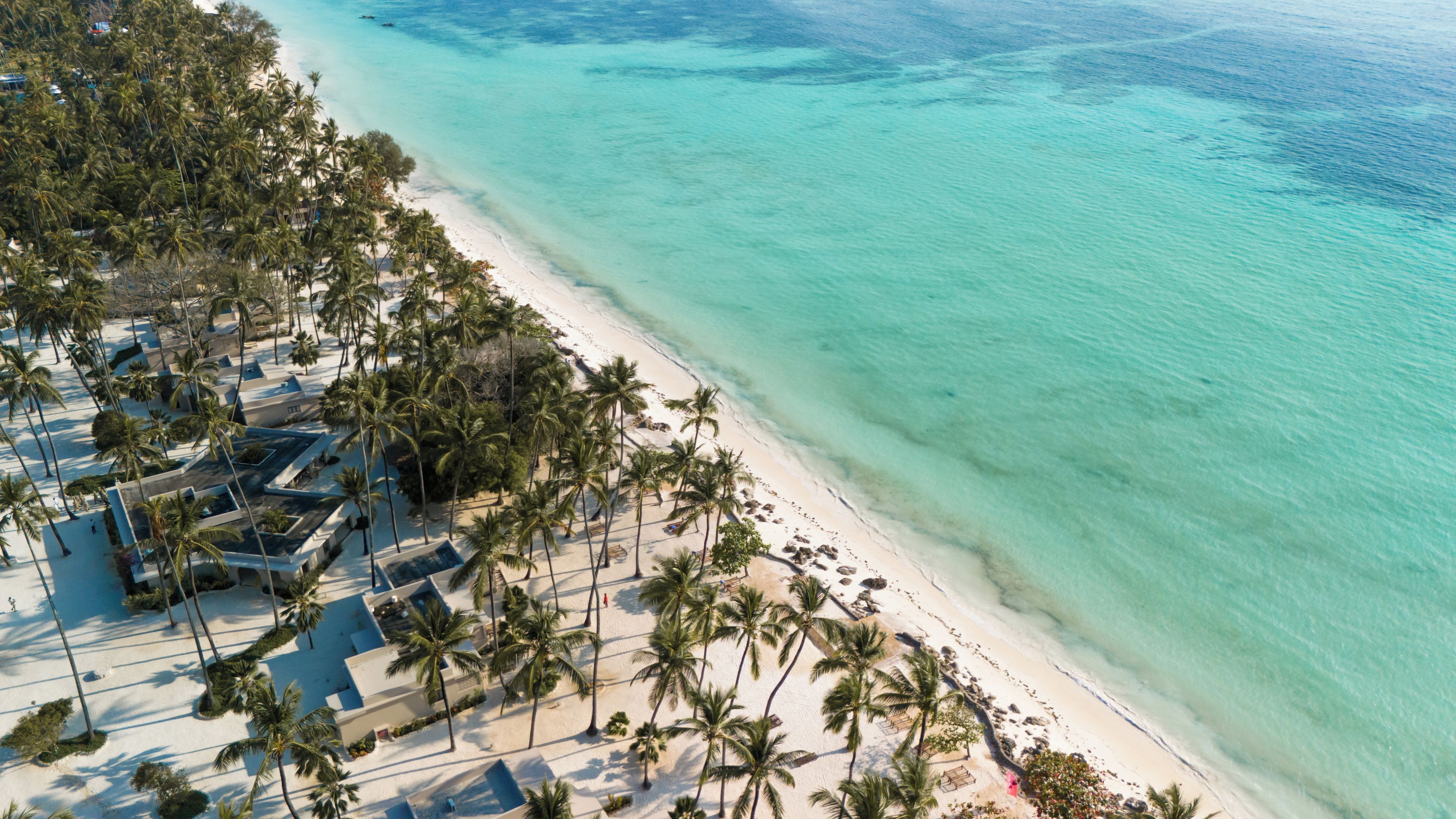 Vista aérea de un resort en la playa con palmeras, una playa de arena y agua turquesa cristalina.