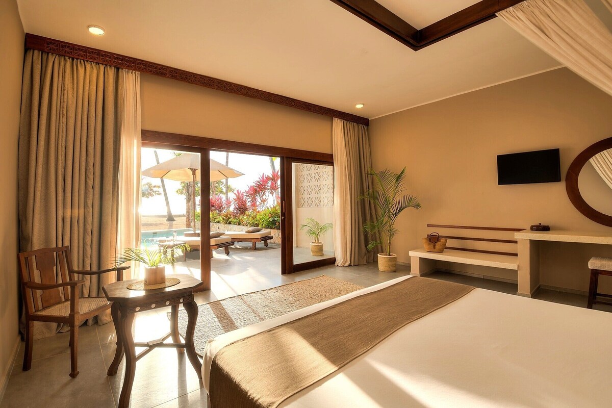 A hotel room with a bed, a desk, a chair, a small table, and a view of the outdoor area.