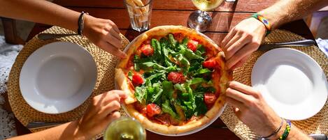 Un grupo de personas alrededor de una mesa con pizza, copas de vino y palitos de pan.