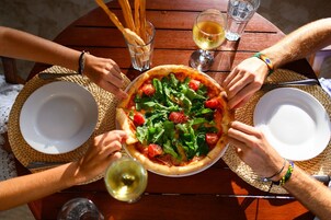 Um grupo de pessoas reunido em torno de uma mesa, com pizza, copos de vinho e palitos de pão.