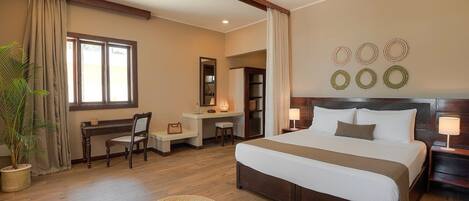 A hotel room with a large bed, a desk, a chair, and a potted plant.