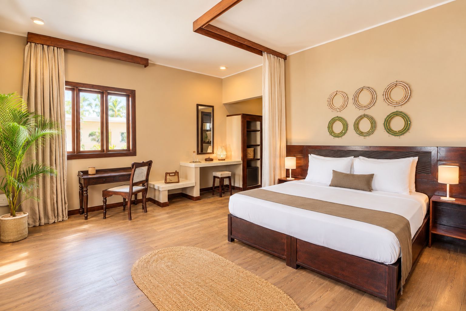 Quarto de hotel com uma cama grande, escrivaninha, cadeira, planta em vaso e vista para palmeiras pela janela.