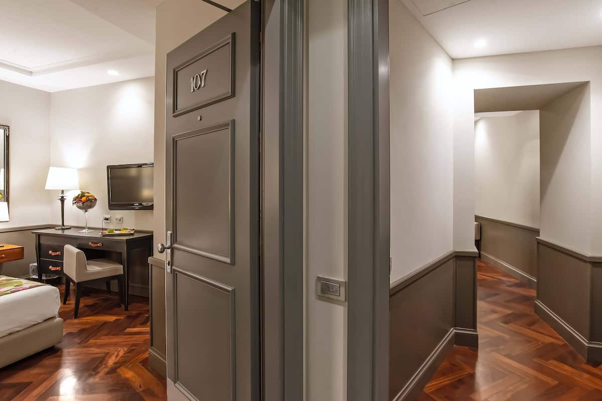 A hotel room with a wooden floor, a desk with a chair, a bed, a TV, and a door with the number 107.