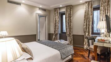 A hotel room with a bed, a desk, a chair, a lamp, and curtains.