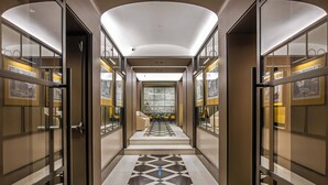 Een moderne hotelgang met glazen deuren, een patroon vloer en een centrale zithoek met uitzicht over de stad.