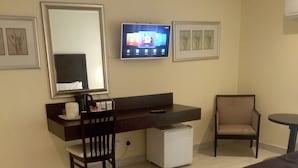 A hotel room with a bed, a desk with a chair, a television, and a small table.