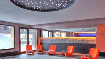 A modern indoor pool area with a circular design, orange lounge chairs, and a ceiling light fixture.