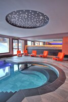 A modern indoor pool area with a circular design, orange lounge chairs, and a ceiling light fixture.