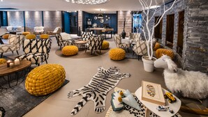 Ein modernes Wohnzimmer mit einer Mischung verschiedener Möbelstücke, darunter gemusterte Sofas und Hocker, ein großer Tigerteppich und ein Zierbaum.
