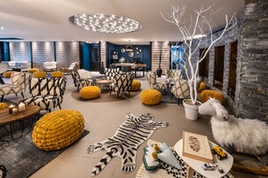 A modern living room with a mix of furniture styles, including patterned sofas and ottomans, a large tiger rug, and a decorative tree.