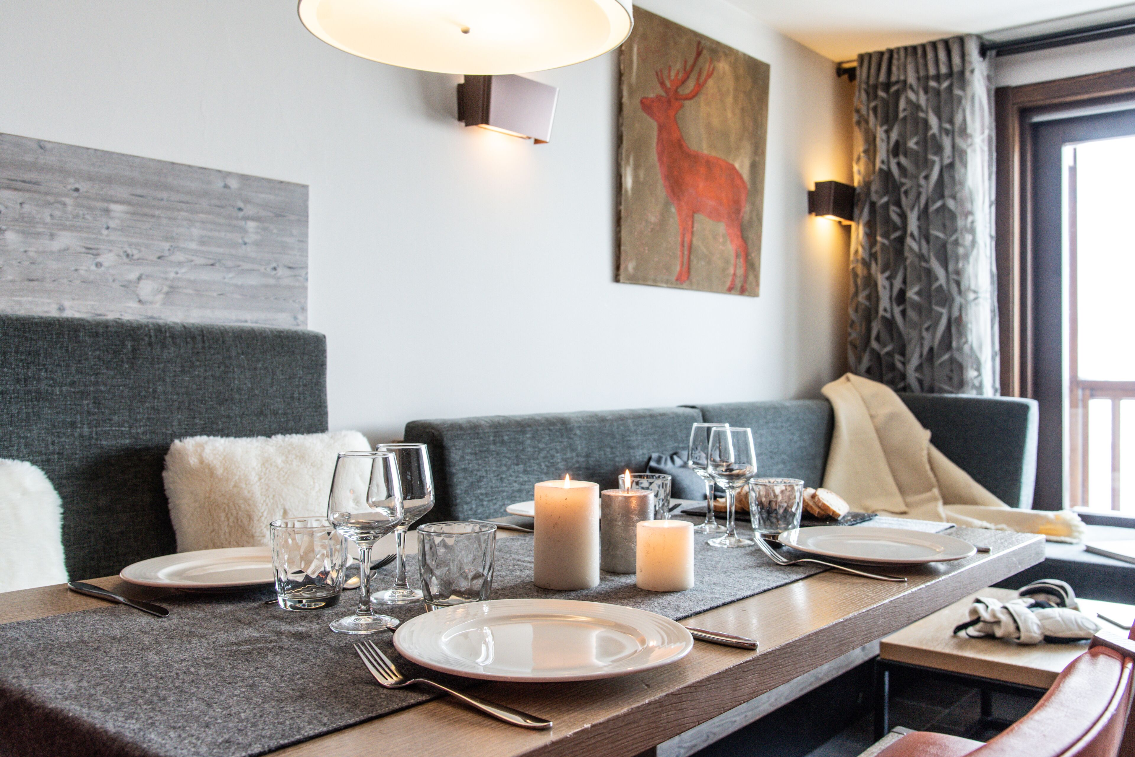 A dining area with a long table set for two, candles, and a wall-mounted painting of a deer.
