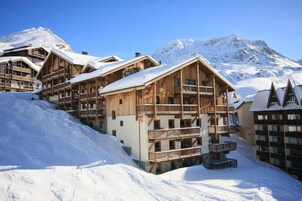 A wooden chalet-style hotel with multiple balconies and a mountain backdrop.