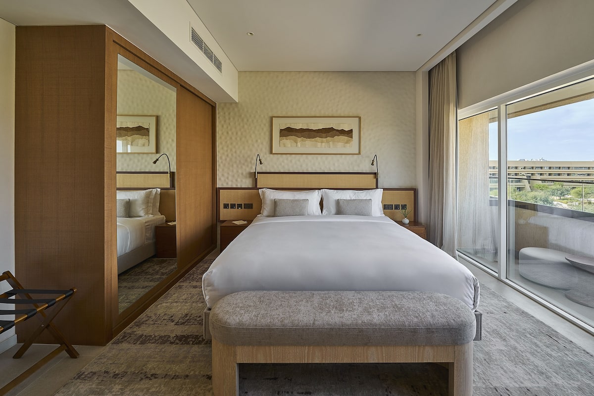 Ein modernes Hotelzimmer mit einem großen Bett, einem Nachttisch, einem Spiegel und einem großen Fenster mit Blick auf die Stadt.