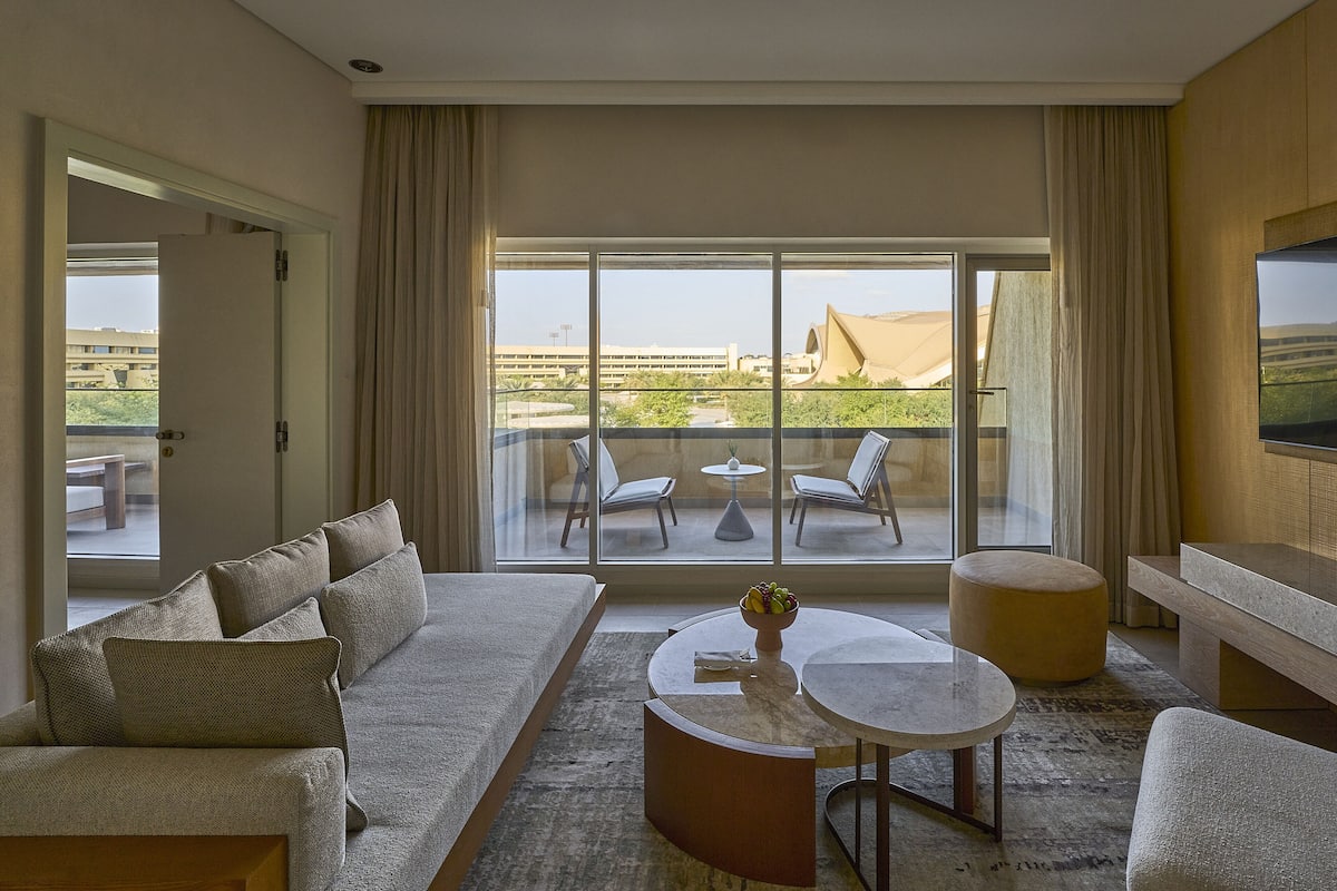Ein modernes Hotelzimmer mit großem Balkon, einer Couch, einem Couchtisch und einem Fernseher.