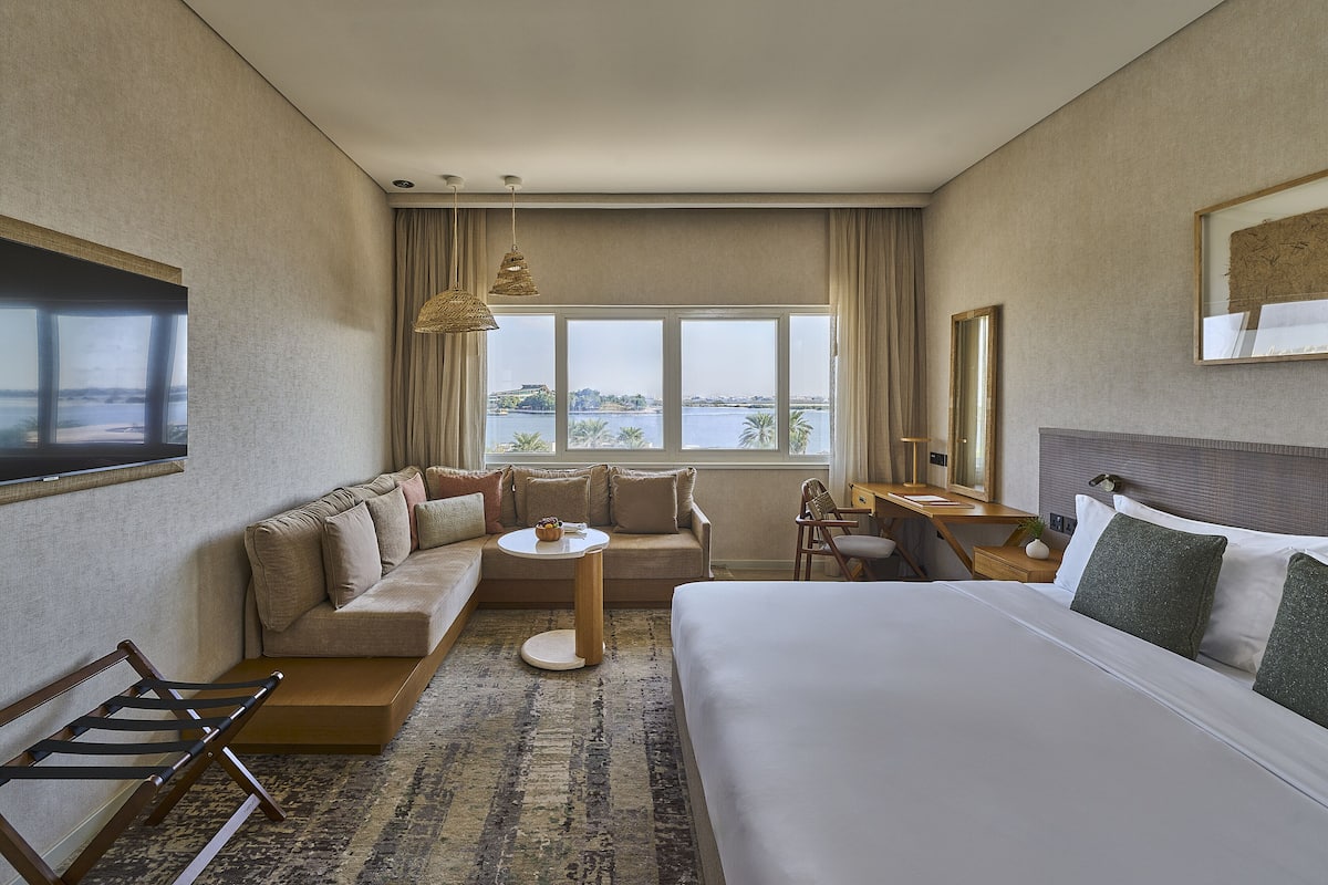 Ein Hotelzimmer mit einem großen Bett, einer Sitzecke, einem Schreibtisch und Blick auf das Wasser.