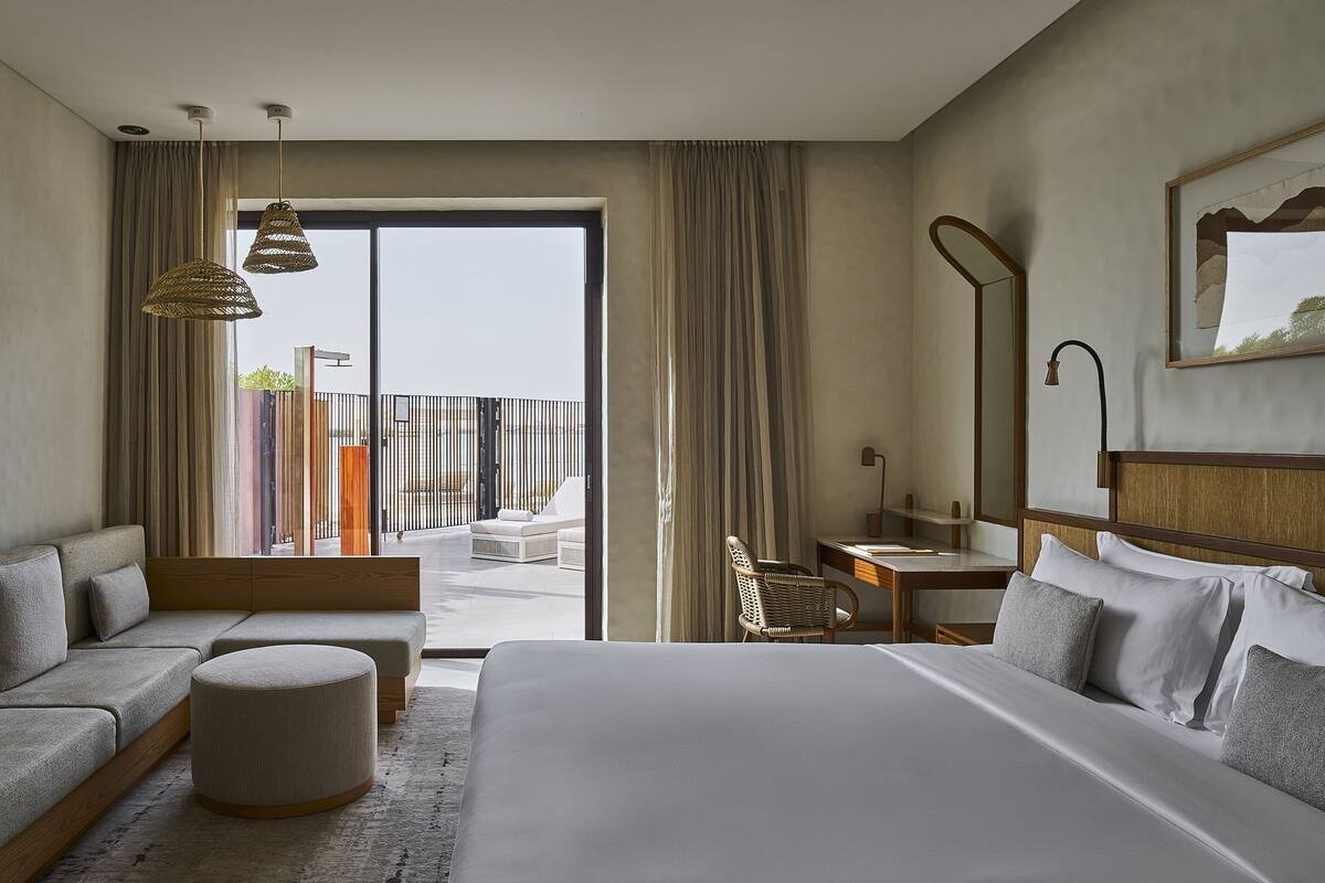 Ein Hotelzimmer mit einem großen Bett, einer Sitzecke, einem Schreibtisch und einem Balkon mit Blick.