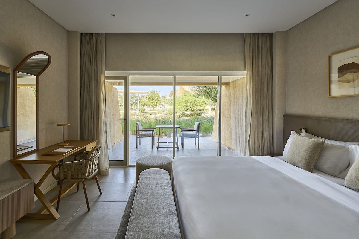 Ein Schlafzimmer mit einem großen Bett, einem Schreibtisch und einem Stuhl. Ein Balkon mit Tisch und Stühlen ist ebenfalls vorhanden.