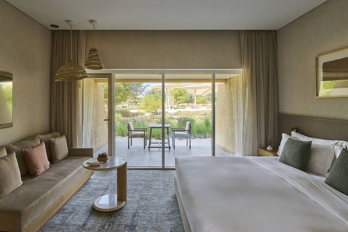 Ein modernes Hotelzimmer mit einem großen Bett, einer Couch, einem kleinen Tisch und einem Balkon mit Blick auf den Garten.