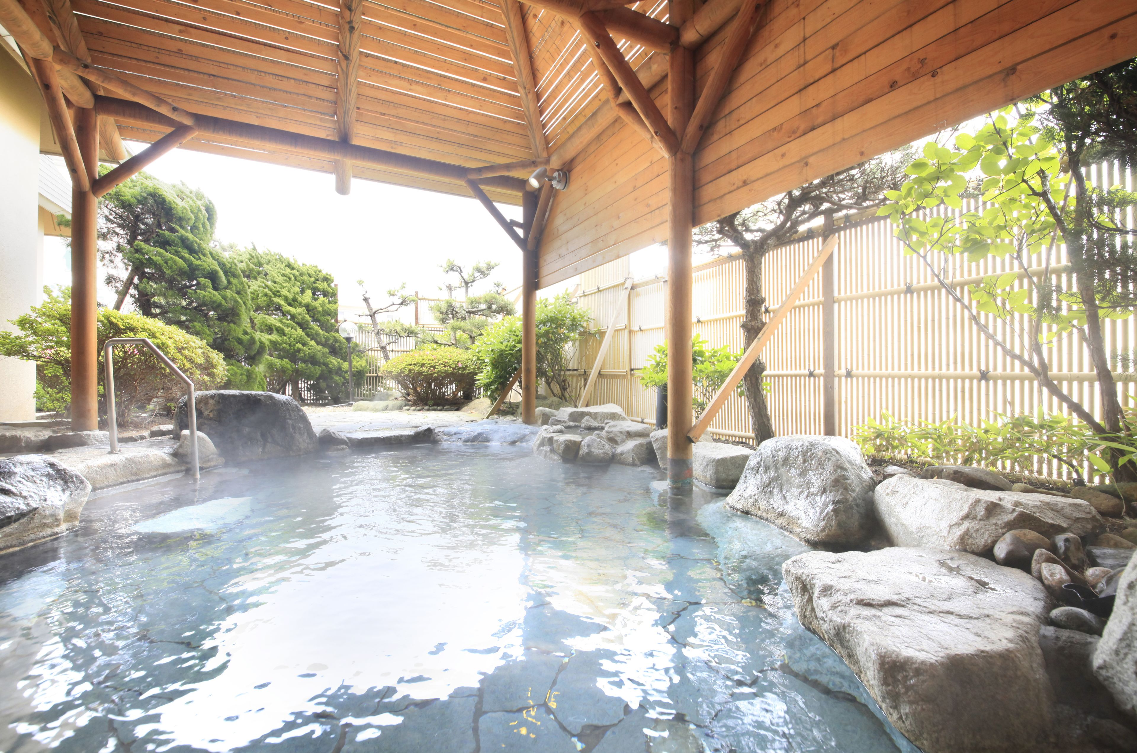 Un onsen japonés tradicional con techo de madera, asientos de piedra y una piscina de piedra natural.