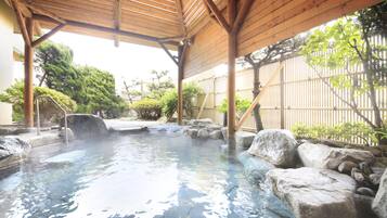 Un onsen japonés tradicional con techo de madera, asientos de piedra y una piscina de piedra natural.