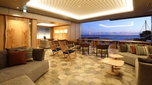 Un salón moderno con vistas al mar, que presenta un techo geométrico, mobiliario de madera y un suelo estampado.