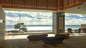 Un interior moderno con vista al océano, que presenta un techo de madera, un ventanal grande y una zona de estar con cojines.