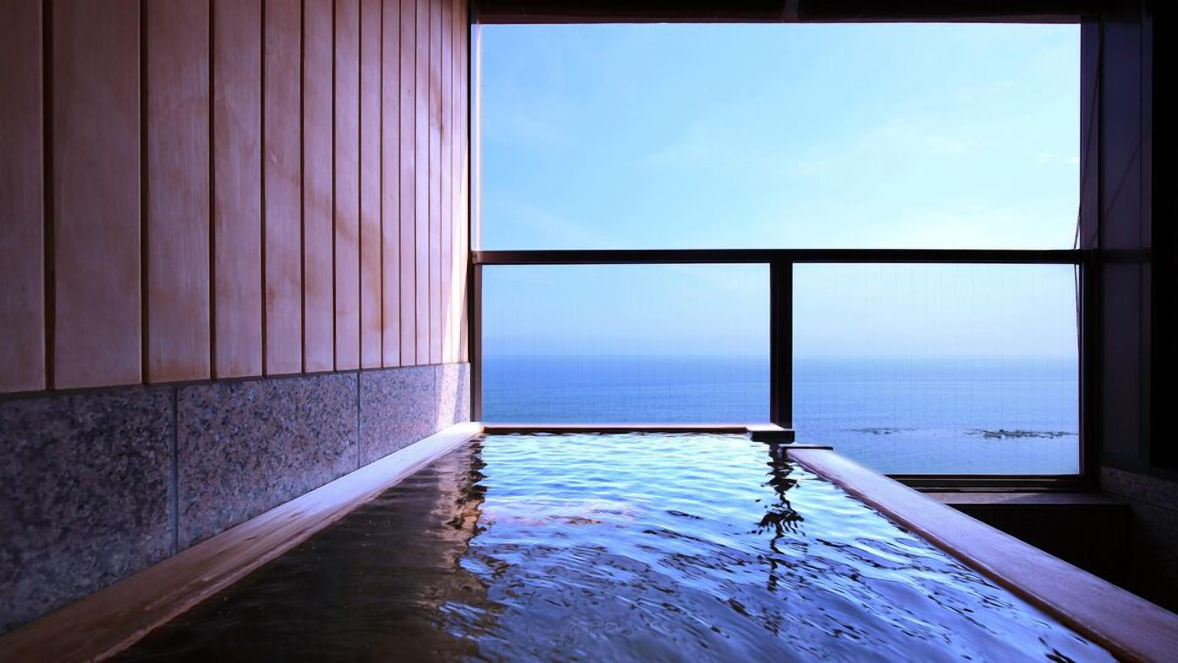 A room with a large window, a wooden floor, and a view of the sea.