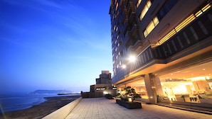Un hotel con terraza frente a la playa, que cuenta con un comedor con mesas al aire libre y vistas al océano.