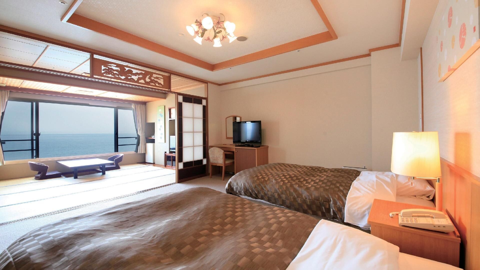 A hotel room with a bed, a desk, a television, and a view of the sea.
