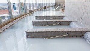 Een modern binnenzwembad met glazen wanden, een trap naar het water en metalen leuningen.