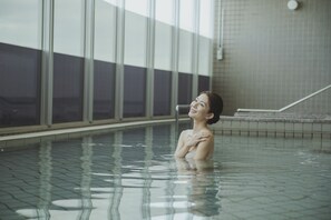 Una persona en una piscina con paredes de azulejos y un ventanal visible.