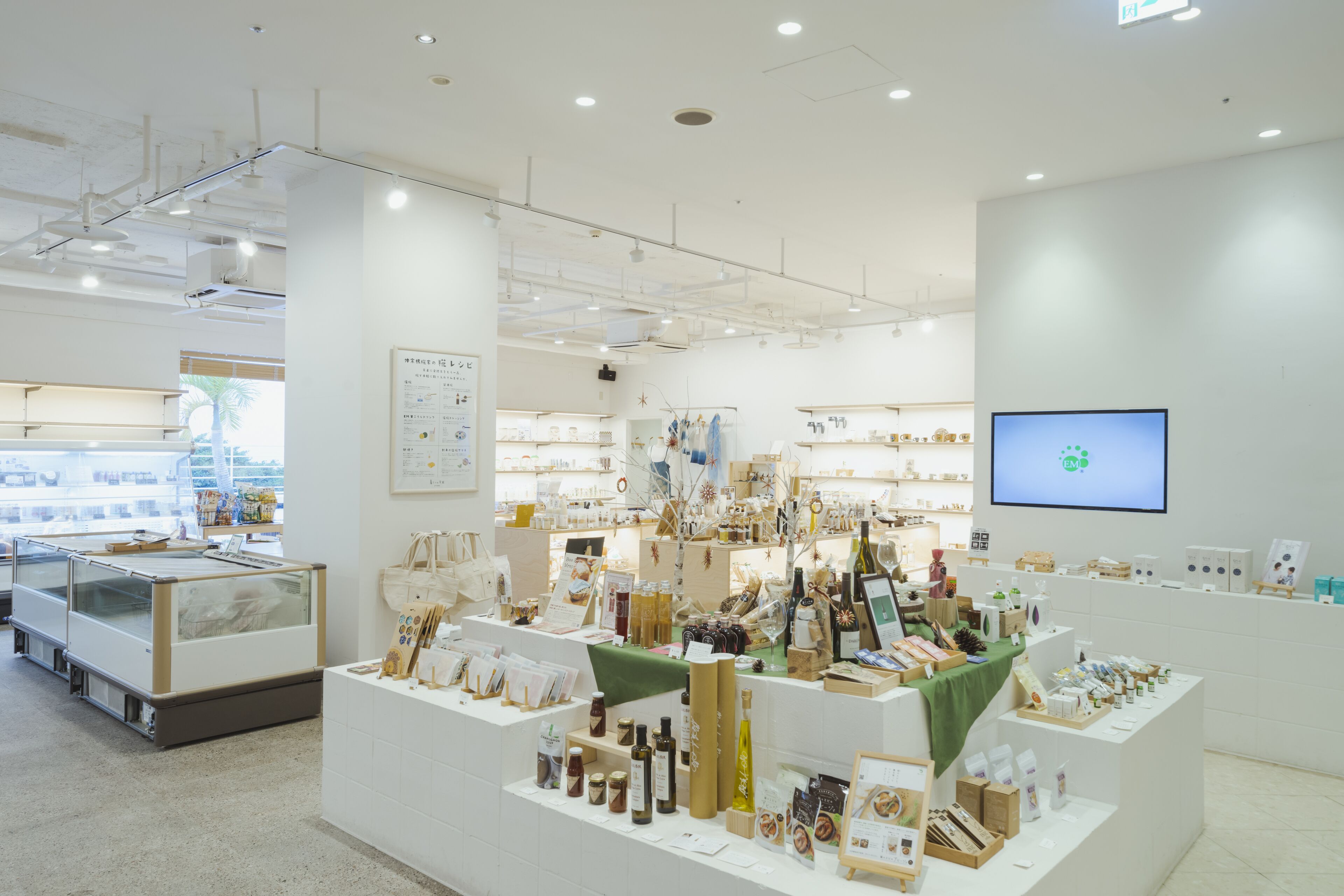 A clean, well-lit store with various products on display, including bottles and boxes, and a television screen on the wall.
