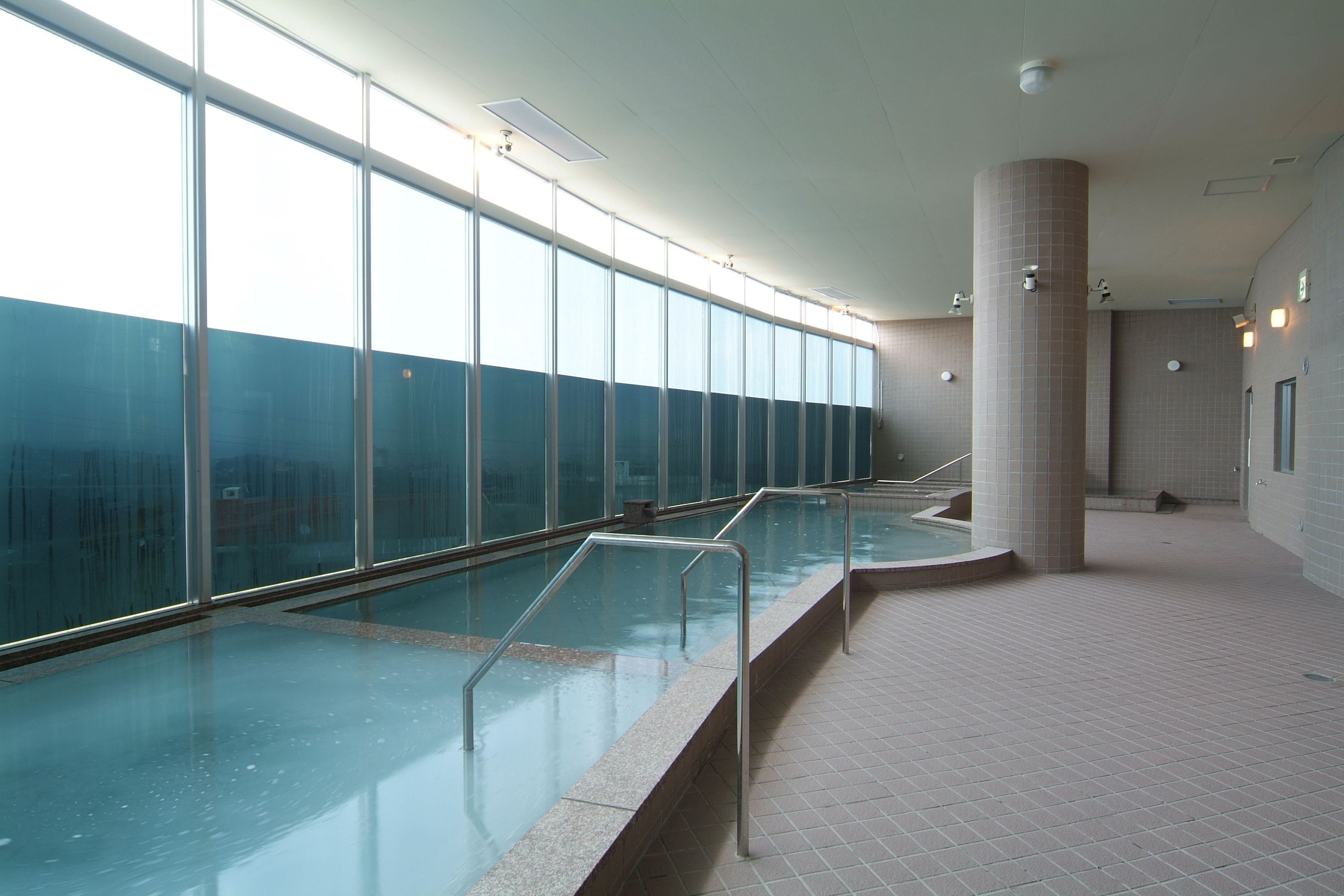 Une piscine dotée de rampes en verre, de grandes fenêtres et de murs carrelés.